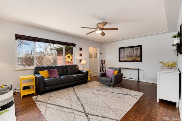 living area with baseboards, dark wood-type flooring, and a ceiling fan