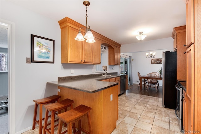 kitchen featuring dark countertops, a chandelier, appliances with stainless steel finishes, a peninsula, and a sink