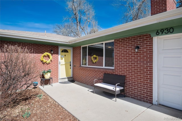 property entrance with brick siding, an attached garage, and a chimney