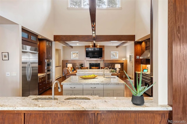 kitchen with a towering ceiling, sink, a tiled fireplace, built in appliances, and light stone counters