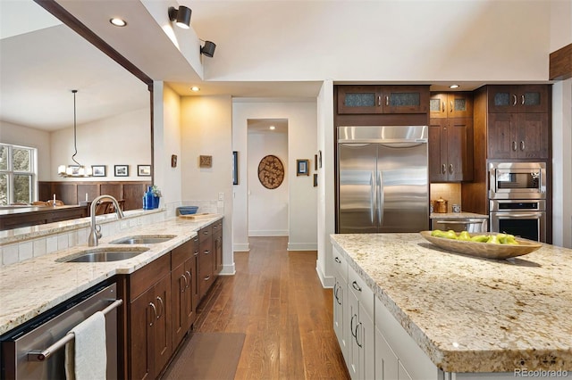 kitchen with tasteful backsplash, sink, hanging light fixtures, built in appliances, and light stone countertops