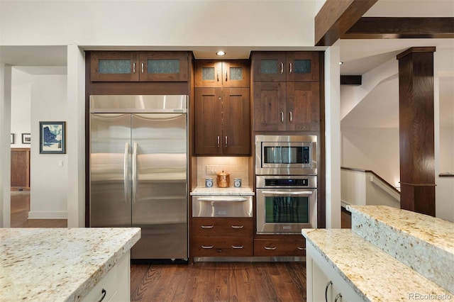 kitchen with built in appliances, backsplash, light stone countertops, and dark hardwood / wood-style floors