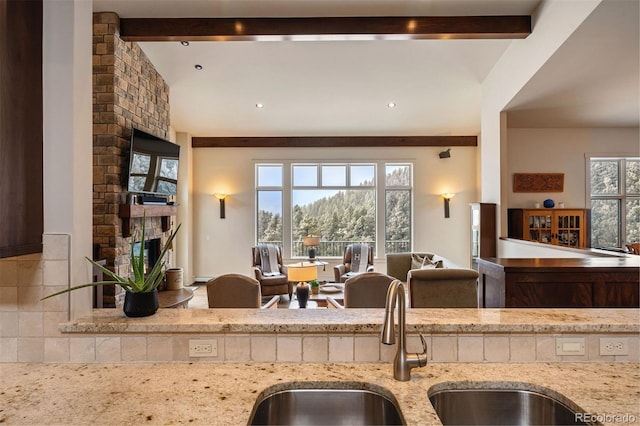 kitchen featuring sink, vaulted ceiling with beams, a fireplace, and light stone counters