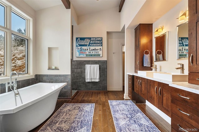 bathroom with a bathing tub, beamed ceiling, tile walls, hardwood / wood-style flooring, and vanity