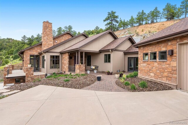 21609 Clarence Ln, Golden, CO 80401 - back of house with stone siding, a chimney, a patio area, and a shingled roof