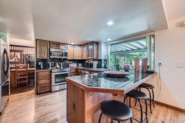 4878 W 98th Ave, Westminster, CO 80031 - kitchen featuring appliances with stainless steel finishes, tile countertops, a breakfast bar area, a peninsula, and light wood-style floors