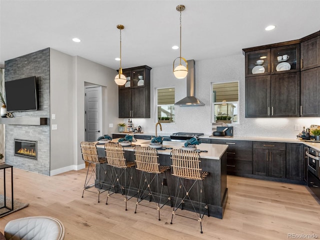 kitchen featuring a center island, wall chimney exhaust hood, light hardwood / wood-style flooring, a kitchen bar, and dark brown cabinets