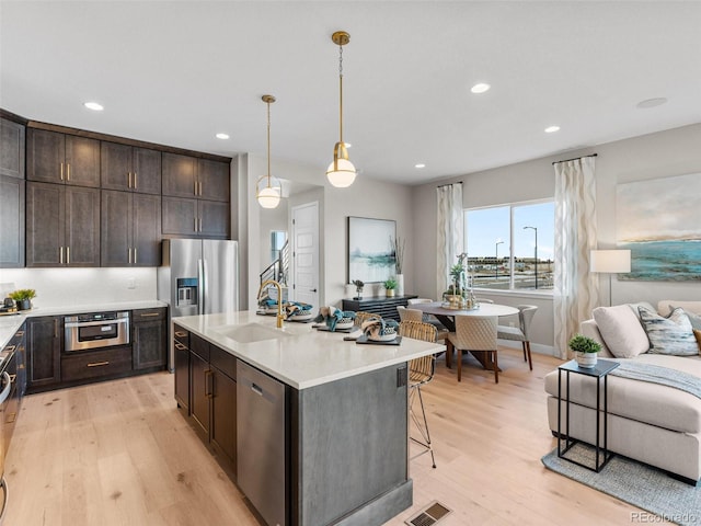 kitchen featuring sink, an island with sink, decorative light fixtures, appliances with stainless steel finishes, and light wood-type flooring