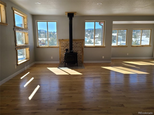 unfurnished living room featuring a wood stove, dark wood-type flooring, a mountain view, and baseboards