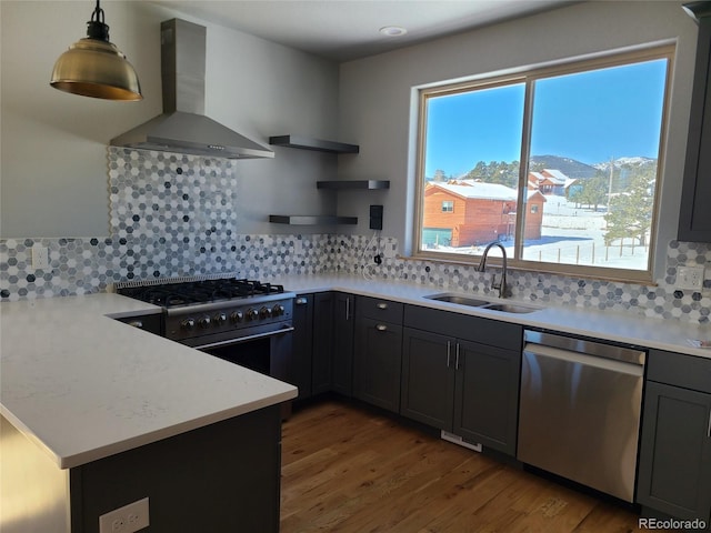 kitchen with decorative light fixtures, a peninsula, stainless steel appliances, wall chimney range hood, and a sink