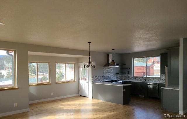 kitchen featuring a peninsula, black dishwasher, light countertops, wall chimney range hood, and tasteful backsplash