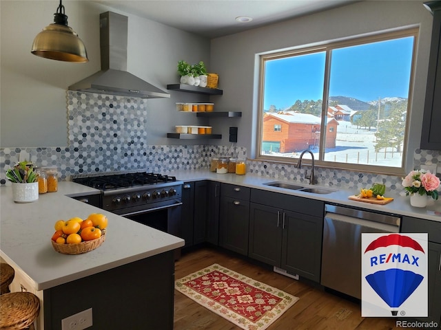 kitchen with wall chimney exhaust hood, appliances with stainless steel finishes, light countertops, pendant lighting, and a sink