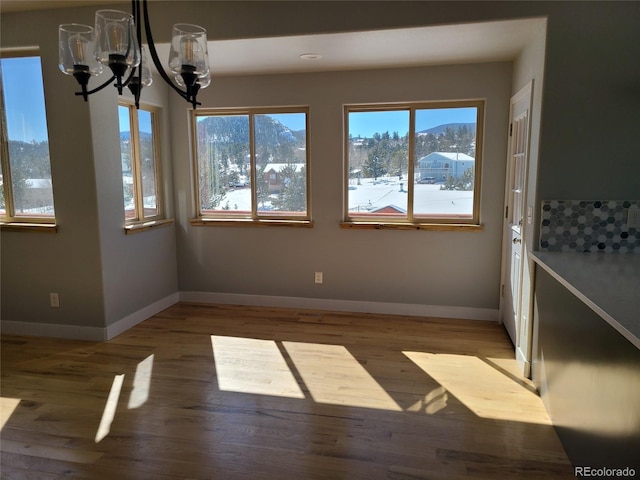 unfurnished dining area with a chandelier, wood finished floors, a mountain view, and baseboards