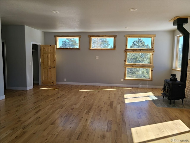 unfurnished living room with a wood stove, baseboards, wood finished floors, and recessed lighting