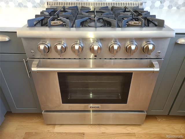 room details featuring high end stove, decorative backsplash, light countertops, and gray cabinetry