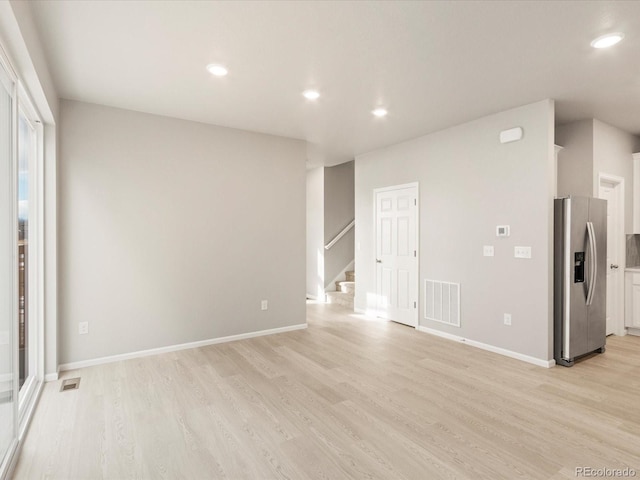 unfurnished living room featuring visible vents, light wood-style flooring, and stairway