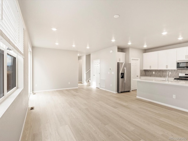 kitchen with stainless steel appliances, light countertops, white cabinets, light wood-style floors, and backsplash