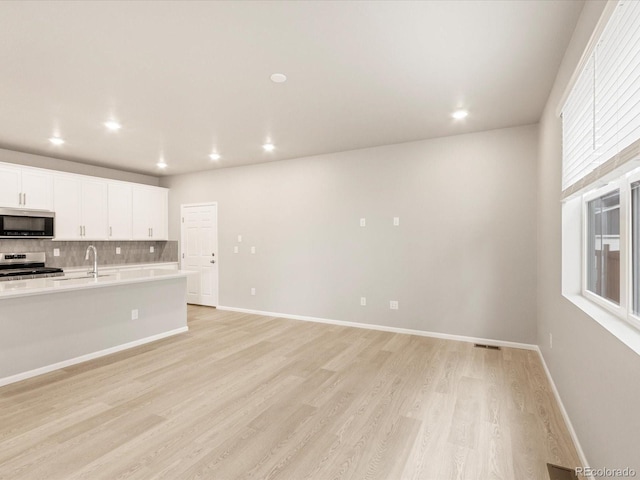 kitchen featuring decorative backsplash, light wood-style flooring, white cabinets, and stainless steel appliances