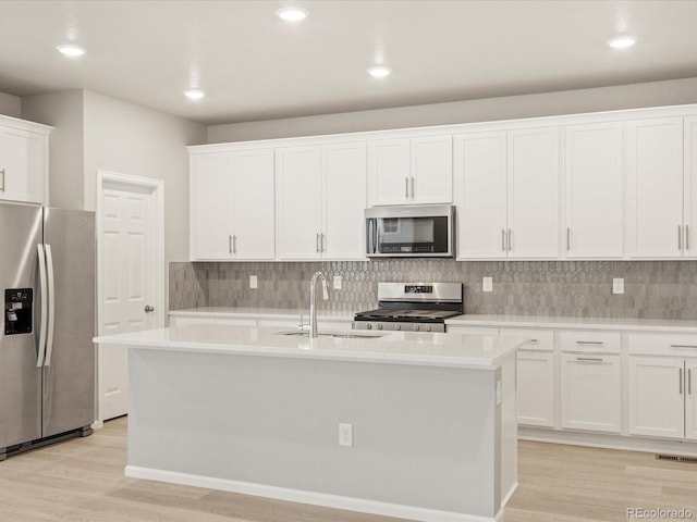 kitchen with light wood-style flooring, an island with sink, stainless steel appliances, light countertops, and tasteful backsplash