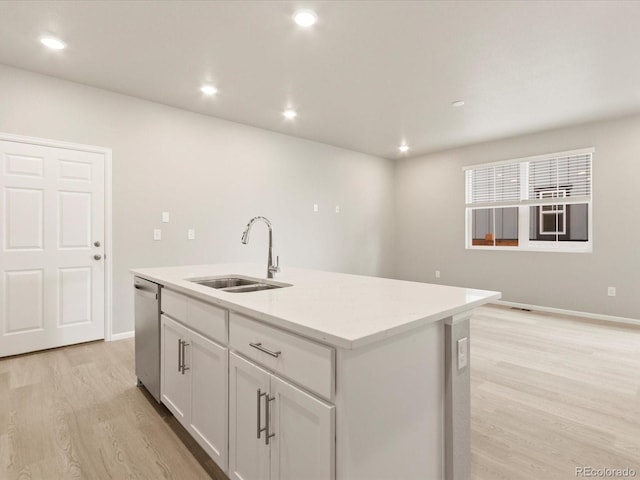 kitchen featuring light wood-type flooring, a kitchen island with sink, a sink, white cabinetry, and dishwasher