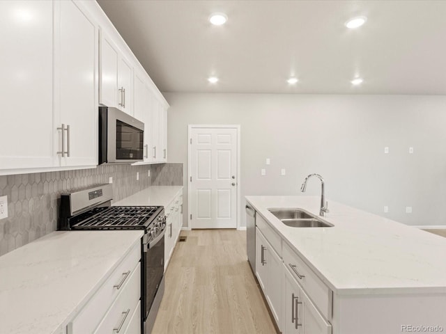 kitchen featuring tasteful backsplash, light wood finished floors, a center island with sink, appliances with stainless steel finishes, and a sink