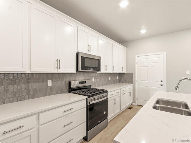 kitchen with light wood finished floors, a sink, decorative backsplash, appliances with stainless steel finishes, and white cabinetry