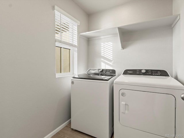 clothes washing area with light wood-style floors, baseboards, separate washer and dryer, and laundry area