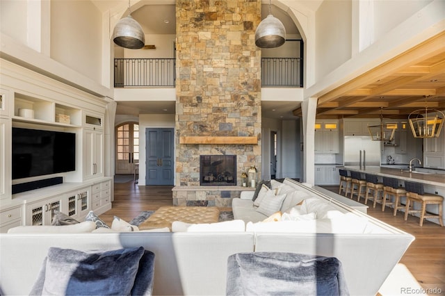 living room with a high ceiling, sink, dark wood-type flooring, and a stone fireplace