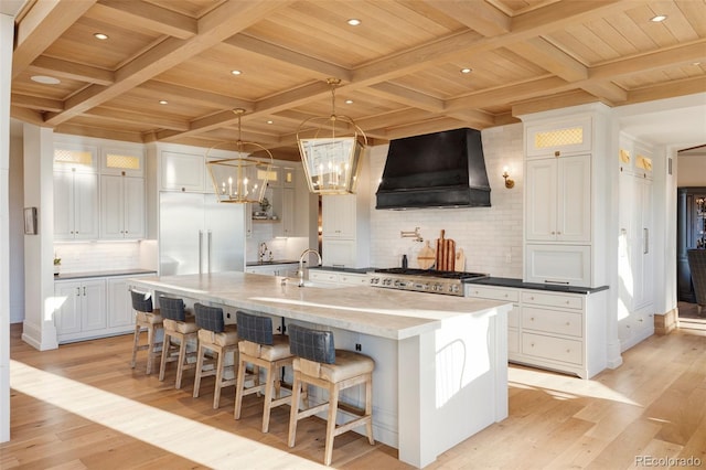 kitchen with white cabinets, wood ceiling, a large island with sink, and custom range hood