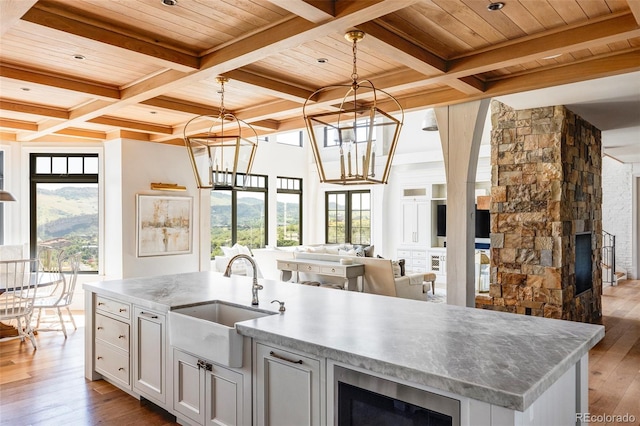 kitchen featuring sink, wooden ceiling, light hardwood / wood-style flooring, an island with sink, and a stone fireplace