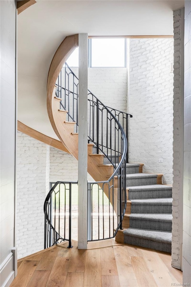 stairway featuring a high ceiling, brick wall, wood-type flooring, and plenty of natural light