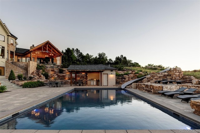 pool at dusk with a patio and a water slide