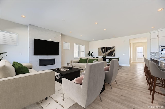 living room with a tiled fireplace and light wood-type flooring