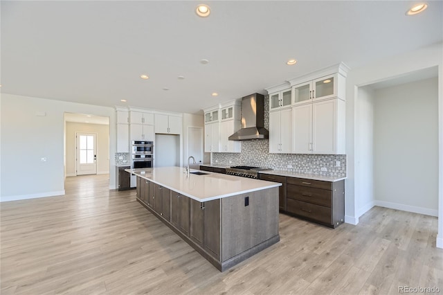 kitchen featuring white cabinets, dark brown cabinets, wall chimney exhaust hood, and an island with sink