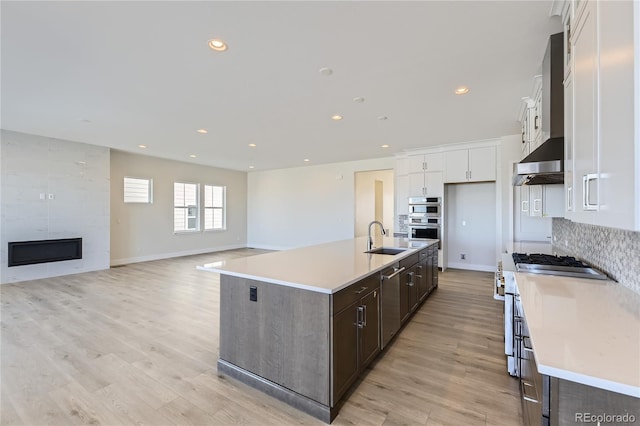 kitchen featuring dark brown cabinets, sink, a fireplace, white cabinetry, and an island with sink