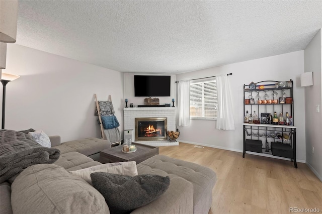 living room with a textured ceiling, a fireplace, and light hardwood / wood-style flooring