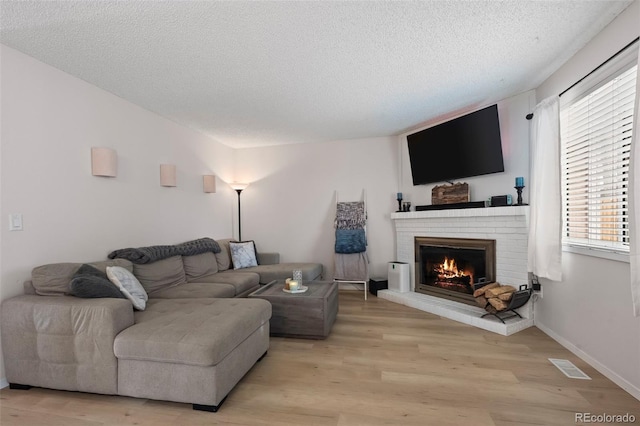 living room featuring a brick fireplace, light hardwood / wood-style floors, and a textured ceiling