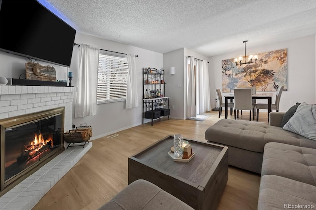 living room with light wood-type flooring, an inviting chandelier, a textured ceiling, and a fireplace