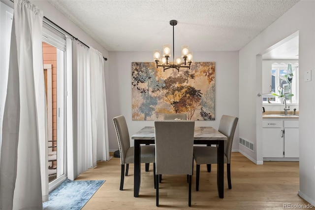 dining room with sink, a notable chandelier, light hardwood / wood-style flooring, and a textured ceiling