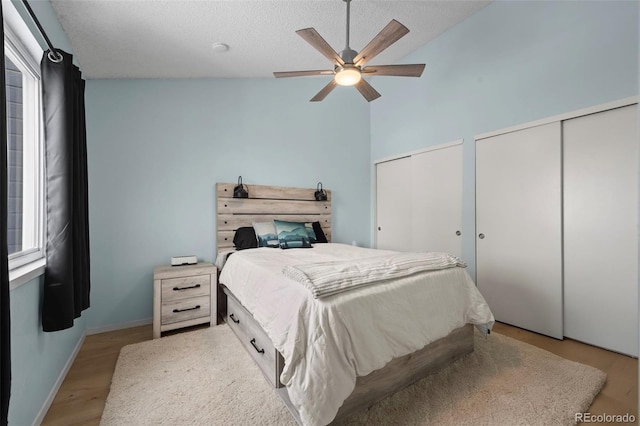 bedroom with ceiling fan, high vaulted ceiling, light hardwood / wood-style floors, a textured ceiling, and two closets