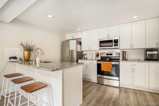 kitchen featuring white cabinets, appliances with stainless steel finishes, a kitchen bar, and light stone countertops