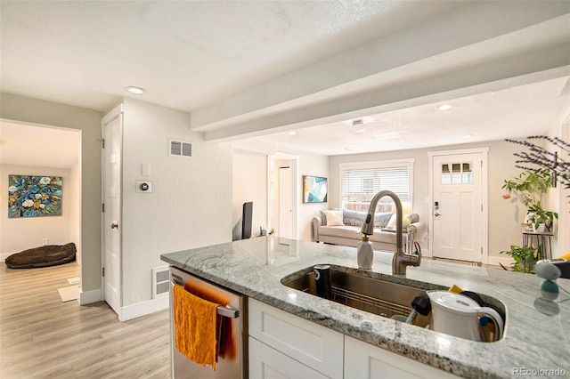 kitchen featuring light stone counters, white cabinets, stainless steel dishwasher, a textured ceiling, and light hardwood / wood-style floors