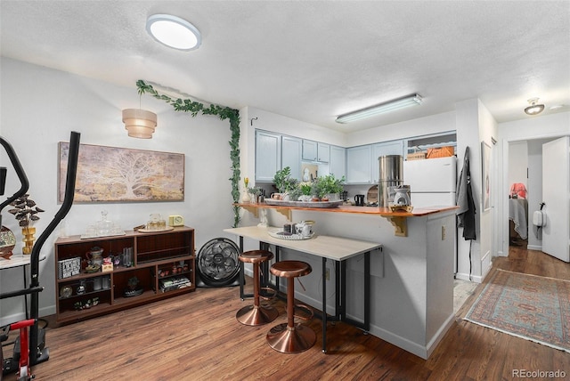 kitchen featuring freestanding refrigerator, wood finished floors, a kitchen breakfast bar, a peninsula, and a textured ceiling