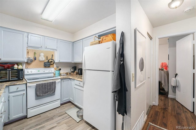 kitchen featuring white appliances, light wood-style floors, light stone counters, and backsplash