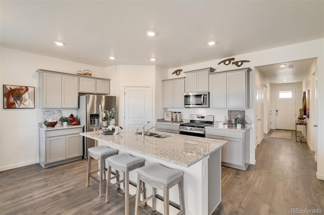 kitchen with appliances with stainless steel finishes, light wood-type flooring, a breakfast bar, gray cabinets, and an island with sink