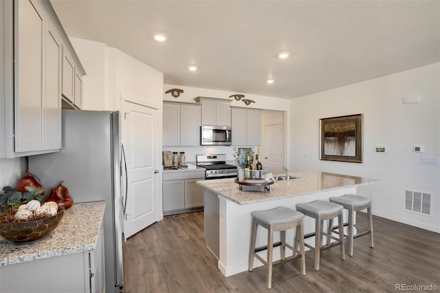 kitchen featuring appliances with stainless steel finishes, light stone counters, sink, a center island with sink, and dark hardwood / wood-style floors