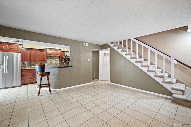 kitchen with a kitchen breakfast bar, stainless steel fridge with ice dispenser, a textured ceiling, decorative backsplash, and light tile patterned floors