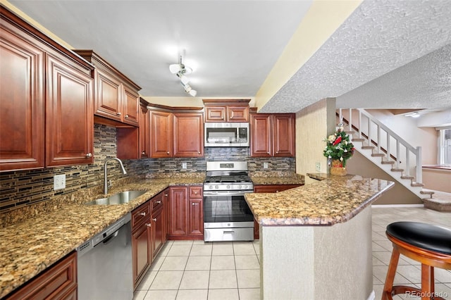 kitchen with sink, kitchen peninsula, a textured ceiling, light tile patterned floors, and appliances with stainless steel finishes