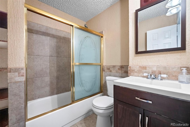 full bathroom featuring combined bath / shower with glass door, vanity, a textured ceiling, tile patterned flooring, and toilet