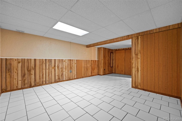 basement featuring wood walls and a drop ceiling